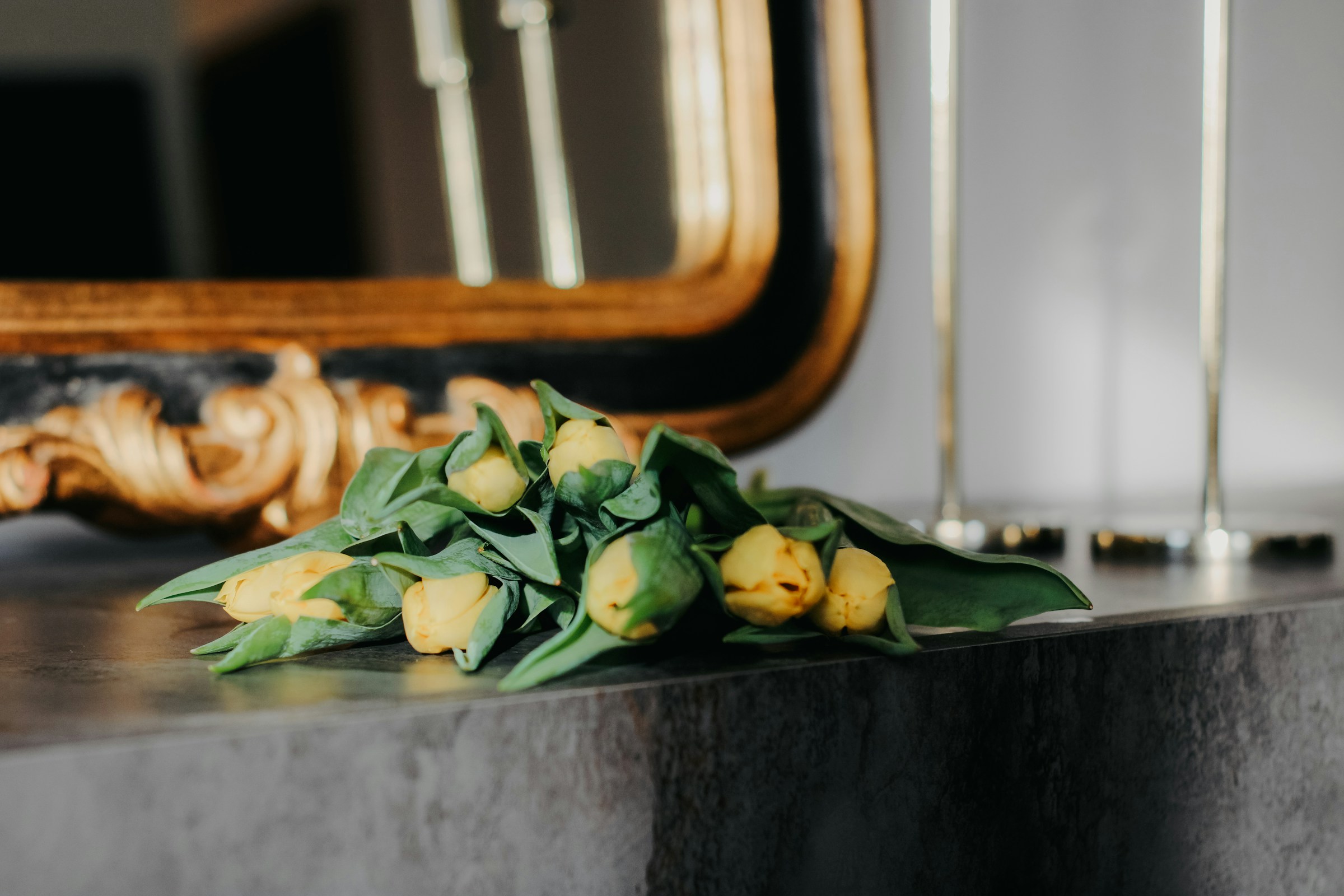 Yellow tulips resting on a dark marble mantel beneath a gilt mirror
